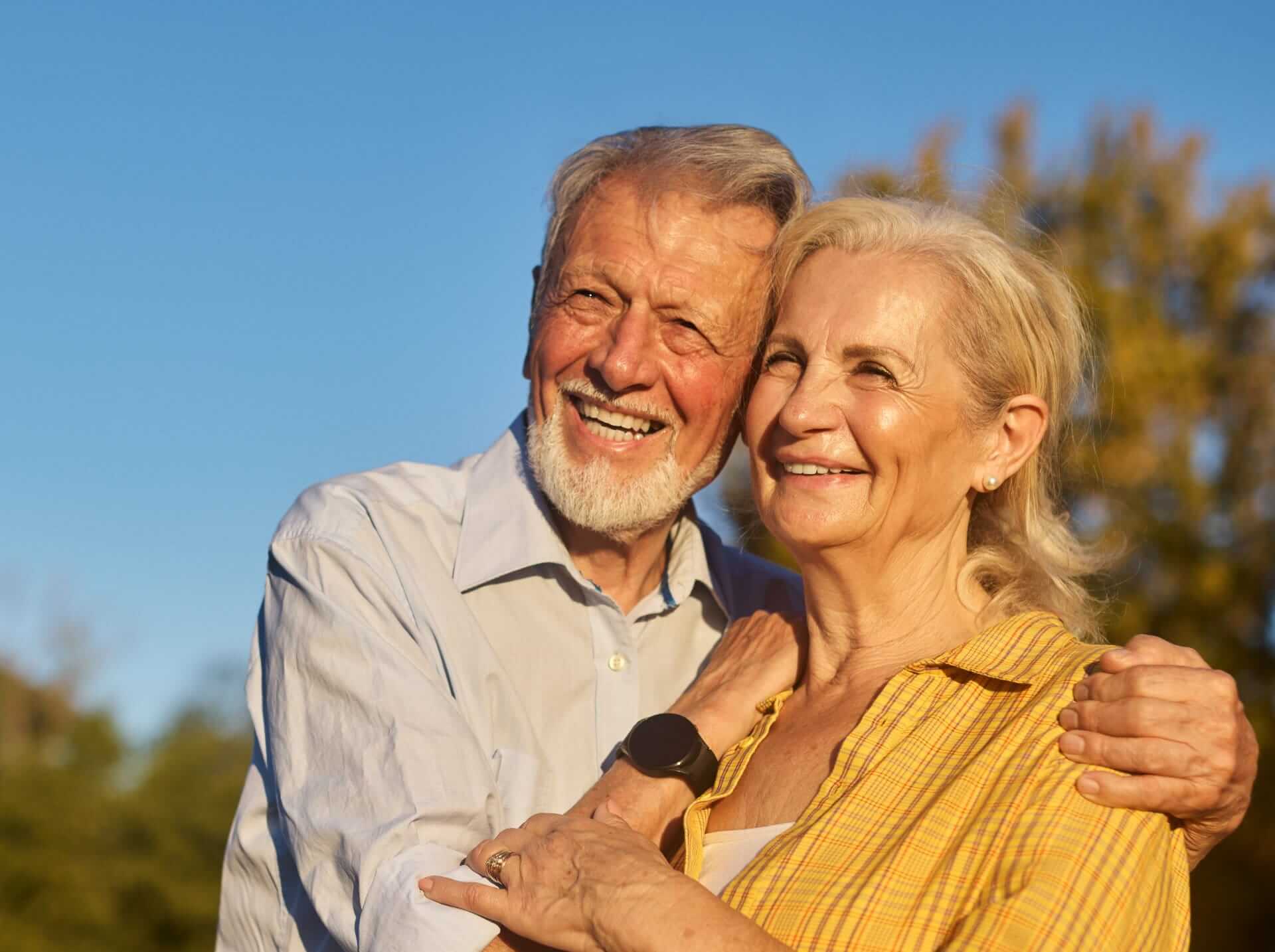 Older couple smiling and embracing outdoors, private healthcare reassurance